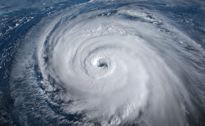 Aerial view of a large, well-formed hurricane with swirling clouds and a distinct eye, moving over an ocean.